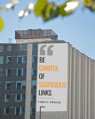 A tall city building with a large billboard that reads “Be careful of suspicious links. #Anti-Fraud.”